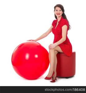 Beautiful woman in red dress sitting on footstool holding a big red balloon  isolated on white background