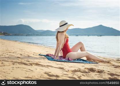 Beautiful woman in red swimsuit is sitting on the beach