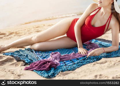 Beautiful woman in red swimsuit is sunbathing on the beach