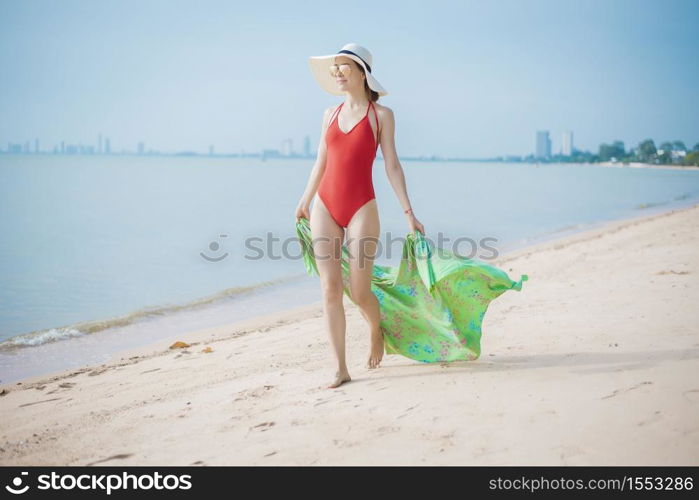Beautiful woman in red swimsuit is walking on the beach