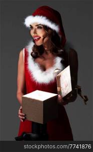 Beautiful woman in santa hat opening glowing magic gift box and smiling. Woman in santa hat opening gift box