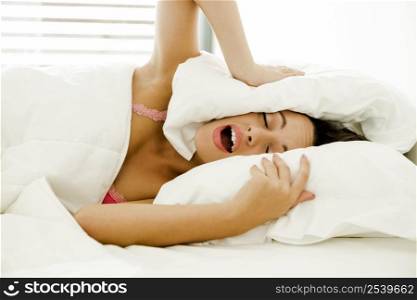 Beautiful woman in the bed and covering her head with a pillow