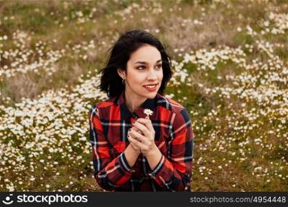 Beautiful woman in the middle of a flowery meadow smelling a daisy