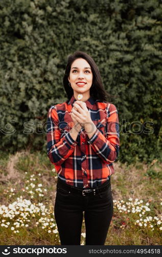 Beautiful woman in the middle of a flowery meadow smelling a daisy