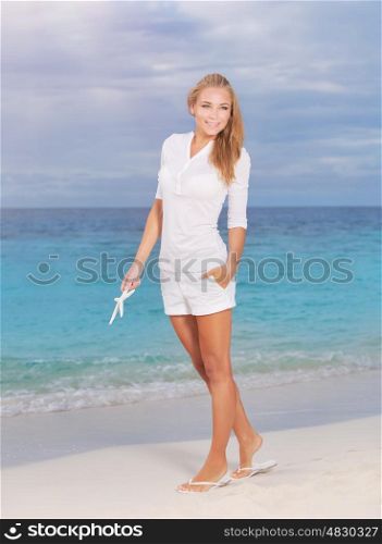 Beautiful woman in vacation, pretty blond girl walking along sandy coast with starfish in hand, enjoying summer holidays on tropical resort