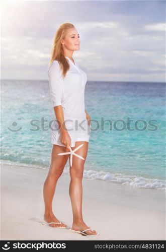 Beautiful woman in vacation, pretty blond girl walking along sandy coast with starfish in hand, enjoying summer holidays on tropical resort
