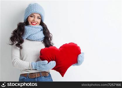 Beautiful woman in warm winter clothes with a big red heart shape pillow , copy space for text , Valentines day , love winter concept. Woman with red heart shape pillow