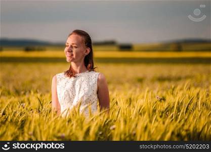 Beautiful woman in white dress on golden yellow wheat field in warm sunshine under dramatic sky, fresh vibrant colors, at Rhine Valley (Rhine Gorge) in Germany
