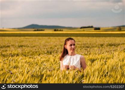 Beautiful woman in white dress on golden yellow wheat field in warm sunshine under dramatic sky, fresh vibrant colors, at Rhine Valley (Rhine Gorge) in Germany