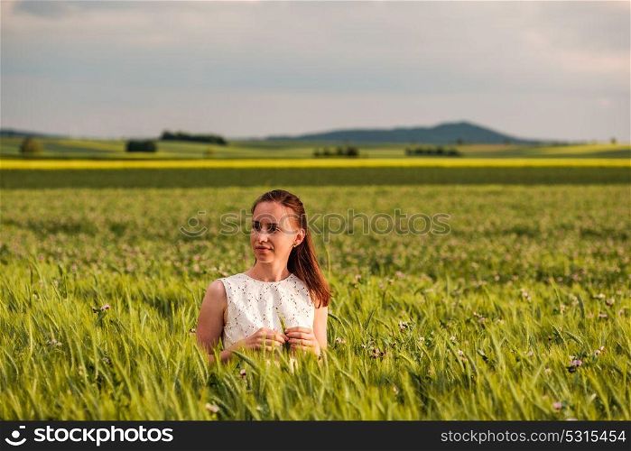 Beautiful woman in white dress on green wheat field in warm sunshine under dramatic sky, fresh vibrant colors, at Rhine Valley (Rhine Gorge) in Germany