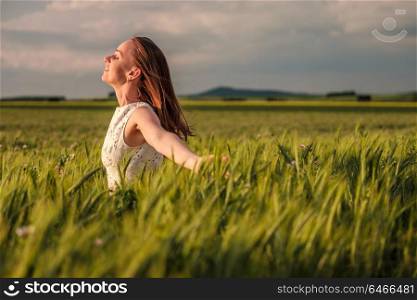 Beautiful woman in white dress on green wheat field in warm sunshine under dramatic sky, fresh vibrant colors, at Rhine Valley (Rhine Gorge) in Germany