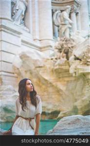 Beautiful woman in white dress sitting in front of Trevi Fountain, Rome, Italy. Happy woman enjoy italian vacation. Holiday in Europe.. Woman in white dress in front of Trevi Fountain in Rome