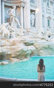 Beautiful woman in white dress sitting in front of Trevi Fountain, Rome, Italy. Happy woman enjoy italian vacation. Holiday in Europe.. Woman in white dress in front of Trevi Fountain in Rome