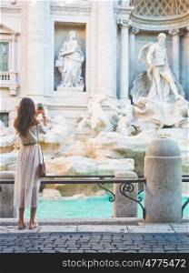 Beautiful woman in white dress take a photo of Trevi Fountain, Rome, Italy. Happy woman enjoy italian vacation. Holiday in Europe.. Woman in white dress in front of Trevi Fountain in Rome
