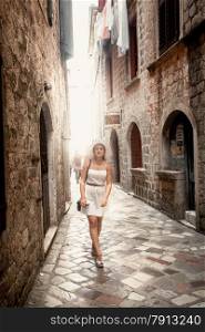 Beautiful woman in white dress walking on narrow street of ancient town