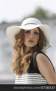 Beautiful woman in white summer hat, looking at camera. She has curly, long, brown hair. Her makeup is so soft.