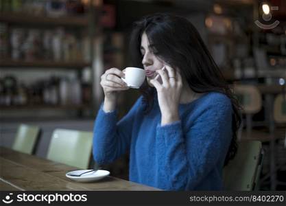 Beautiful woman is drinking delicious coffee while sitting in the bar while talking by phone
