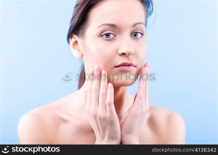 beautiful woman is looking at camera and touching her face on blue background