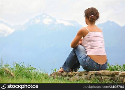 beautiful woman is sitting on a stones and looking at mountains.