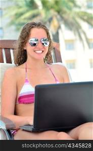 beautiful woman is sitting on wooden chair near the pool with laptop