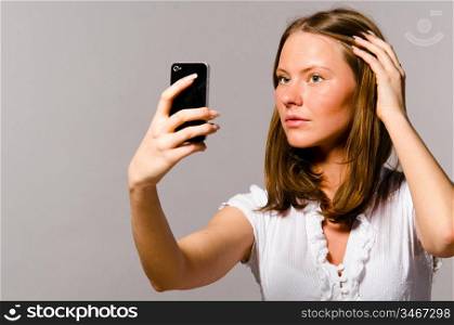 beautiful woman is taking picture of herself with mobile phone on gray background
