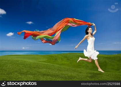 Beautiful woman jumping on a green meadow with colored tissues