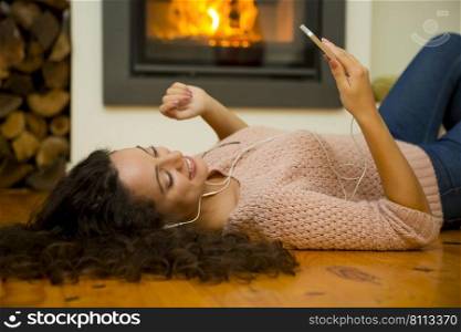 Beautiful woman listen music at home at the warmth of a fireplace