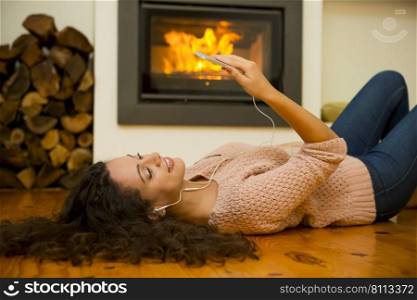 Beautiful woman listen music at home at the warmth of a fireplace