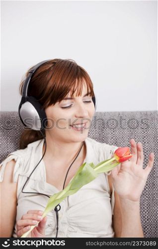 Beautiful woman listening music and holding a orange tuliip on the hands