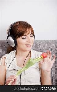 Beautiful woman listening music and holding a orange tuliip on the hands