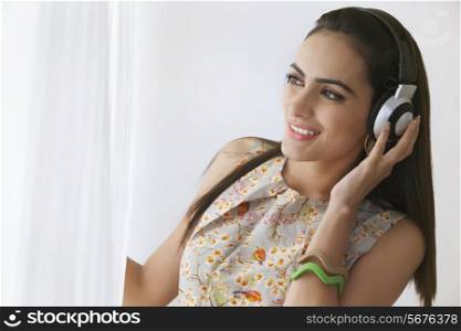 Beautiful woman listening to headphones while looking through window