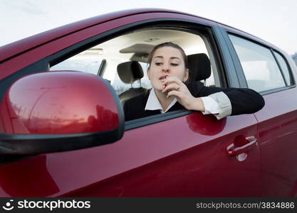 Beautiful woman looking in car side mirror and applying lipstick