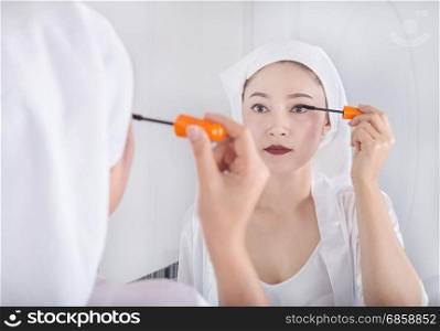 Beautiful woman looking mirror and applying mascara on her eyelashes