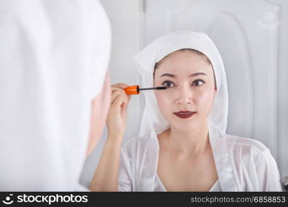 Beautiful woman looking mirror and applying mascara on her eyelashes