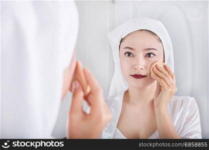 Beautiful woman looking mirror and applying powder foundation on face