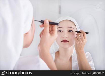 Beautiful woman looking mirror and make-up with black eyeliner