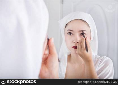 Beautiful woman looking mirror and using pencil makeup eyebrow
