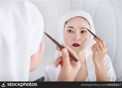 Beautiful woman looking mirror and using pencil makeup eyebrow
