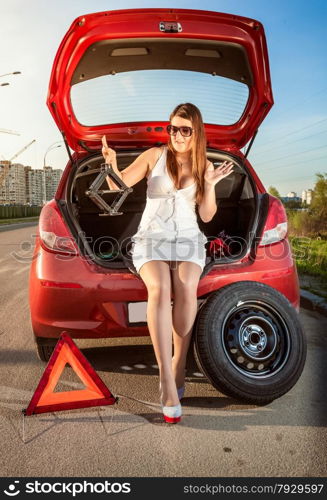 Beautiful woman looking on jack screw near car with punctured wheel