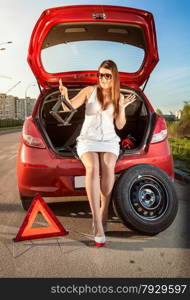 Beautiful woman looking on jack screw near car with punctured wheel