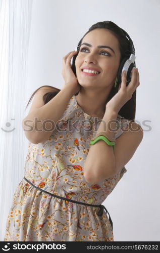 Beautiful woman looking up while listening to headphones by curtain