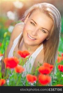 Beautiful woman lying down on fresh red poppy flowers field, enjoying beauty of countryside nature, relaxation and pleasure in the summer garden