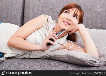 Beautiful woman lying on sofa thinking amd holding a cellphone