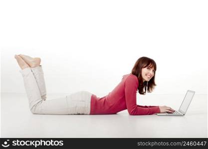Beautiful woman lying on the floor and looking to the camera while working with a laptop