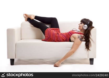 Beautiful woman lying on the sofa and listen music with headphones, isolated on white