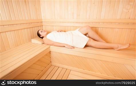 Beautiful woman lying with closed eyes on bench at sauna