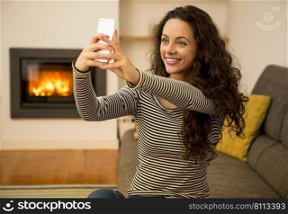 Beautiful woman making a selfie at home at the warmth of a fireplace