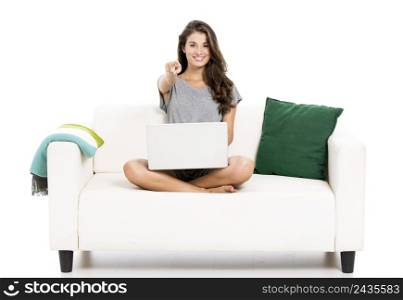 Beautiful woman on a sofa with a laptop and pointing to you, isolated in white