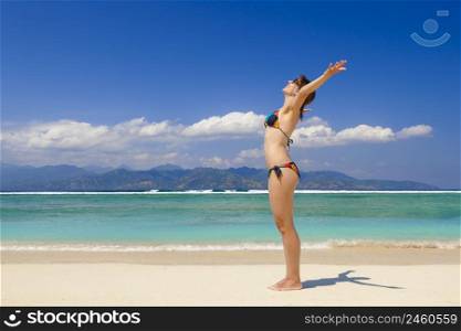 Beautiful woman on a tropical beach with arms open enjoying the summer