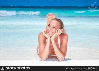 Beautiful woman on the beach, lying down and tanning on a white sandy seashore, enjoying summer vacation on a tropical beach resort